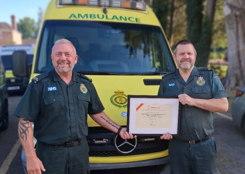 Two members of the Driver Training Department stand in front of an ambulance holding the award certificate