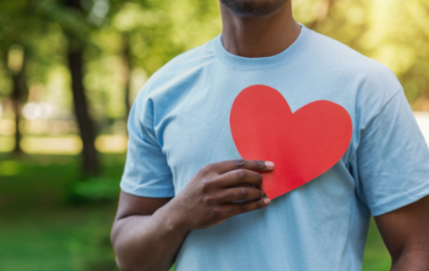 Someone in a blue t-shirt holding a paper red heart over their chest