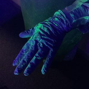 A PPE glove under ultraviolet light reveals the training spray used to mimic contamination.