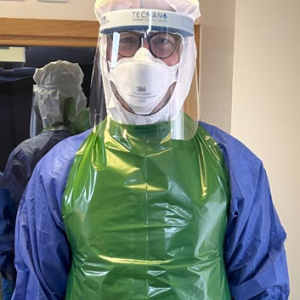 A man facing the camera wearing the PPE ensemble, including apron and face screen