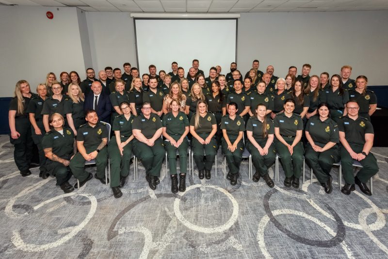 Group of people in green ambulance uniform are stood and seated in rows at awards ceremony