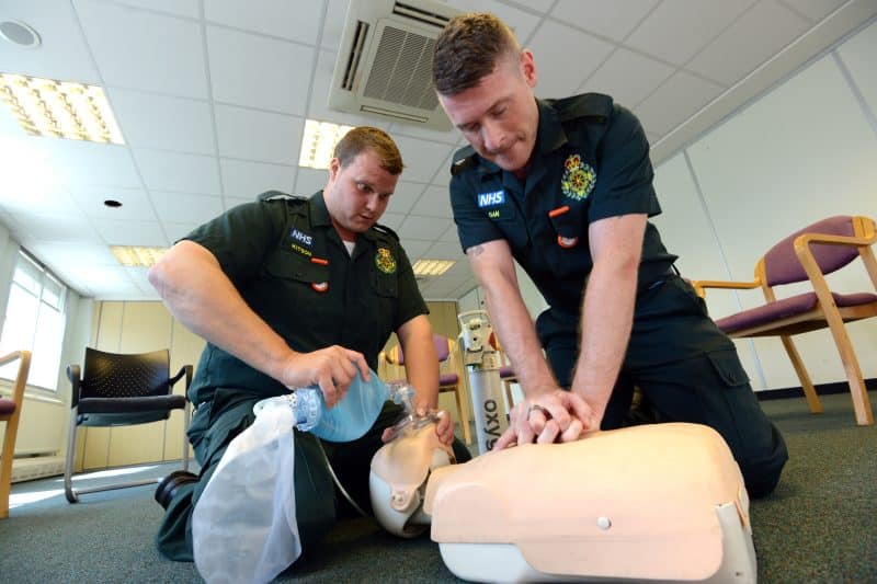 Two ambulance clinicians performing CPR and airway management on a CPR dummy.