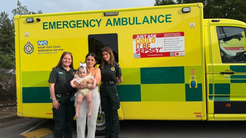 A mum and daughter standing in front of an ambulance with two paramedics wearing green
