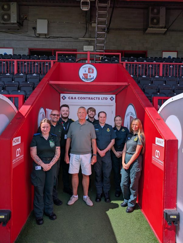 SECAmb colleagues and a cardiac arrest survivor pose in the tunnel at Crawley Town FC stadium.