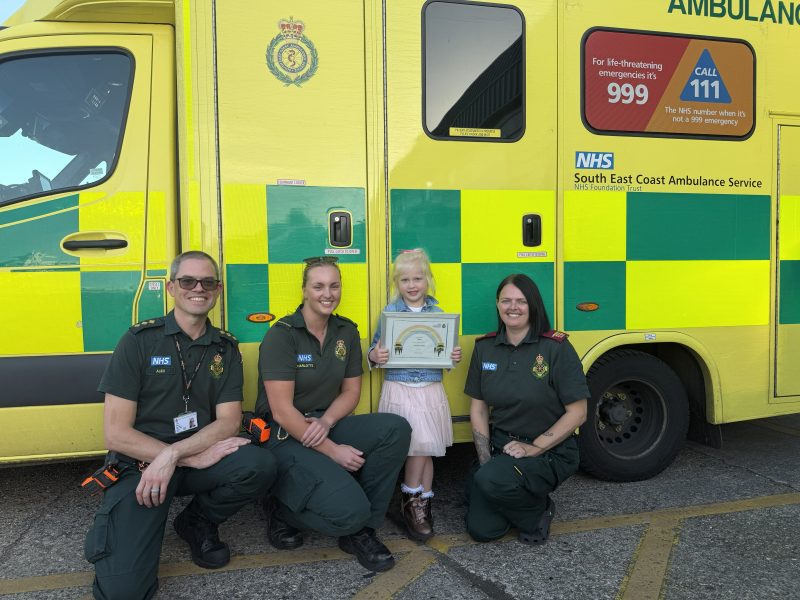 Ambulance clinicians in front of ambulance with little girl holding a certificate