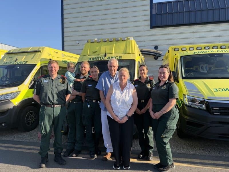 Patient and his wife standing outside an ambulance with paramedics in green